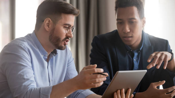 istock Serious african and caucasian coworkers using digital tablet discussing strategy 1254063693