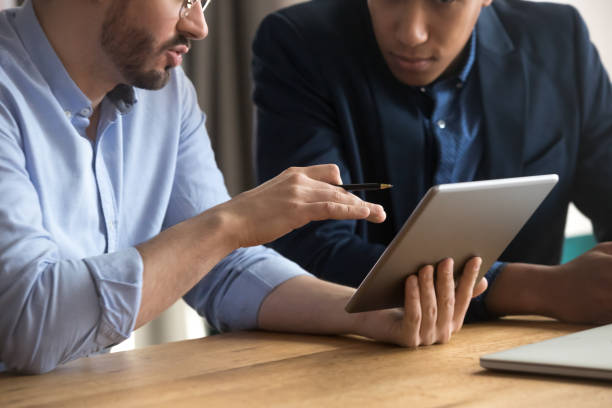 istock Diverse businessmen talking using digital tablet sit at desk, closeup 1254063705