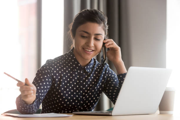 istock Smiling indian business woman talk on phone write notes 1254063727