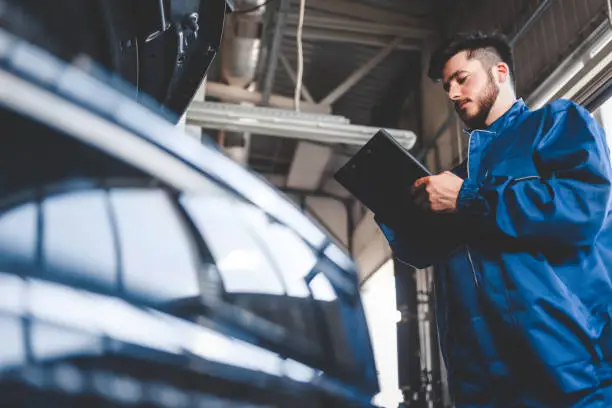 Photo of Car mechanic writes repair plan on clipboard. Auto service worker male