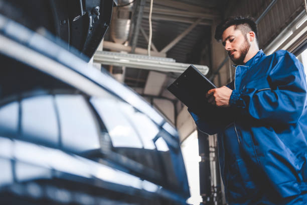 car mechanic writes repair plan on clipboard. auto service worker male - auto repair shop adult auto mechanic blue imagens e fotografias de stock
