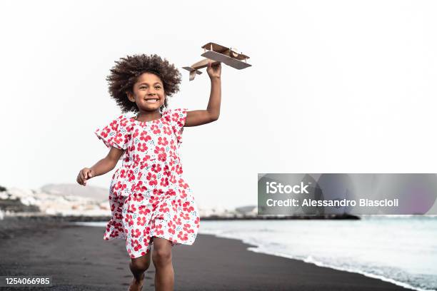 Afro Child Playing With Wood Toy Airplane On The Beach Little Kid Having Fun During Summer Holidays Childhood And Travel Vacation Concept Stock Photo - Download Image Now