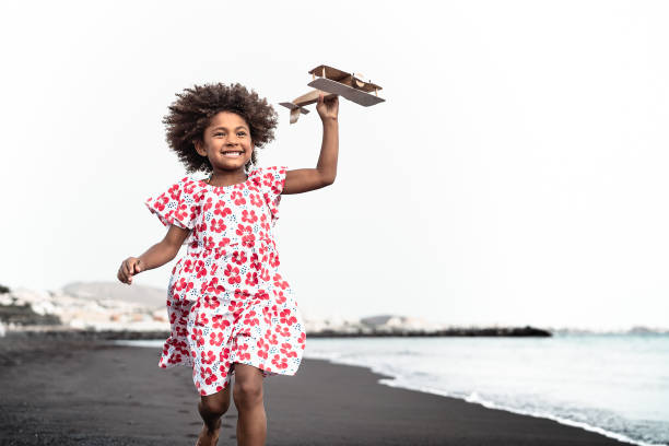 афро ребенок играет с деревянной игрую самолет на пляже - маленький ребенок весело во время летних каникул - детство и путешествия отпуск ко - african descent child little girls african ethnicity стоковые фото и изображения