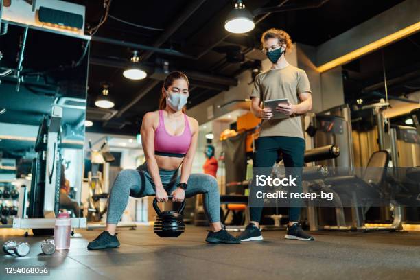 Fitness Trainer Checking Condition Of Female Athlete In Gym While Both Of Them Wearing Protective Face Masks For Illness Prevention Stock Photo - Download Image Now