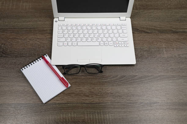 istock A white laptop, Notepad, pen, and glasses on a dark wooden table. 1254069561
