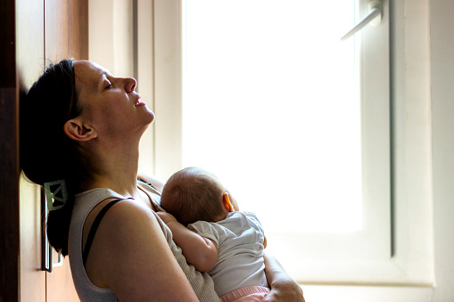 Mother embracing her baby girl while sleeping,lifestyle concept.Tired concerned mother rocking sleeping baby in kitchen.Portrait of young woman and cute little baby in home interior.Motherhood concept