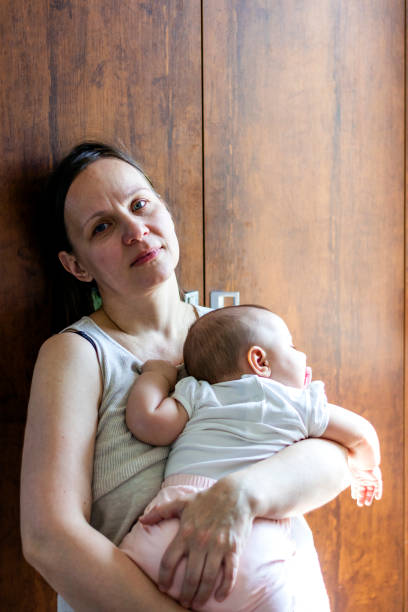 istock Exhausted mother stands in the kitchen holding baby 1254070800