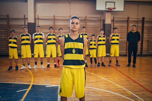 Group of teenage boys, teenage boy basketball player standing in front of his teammates and coach
