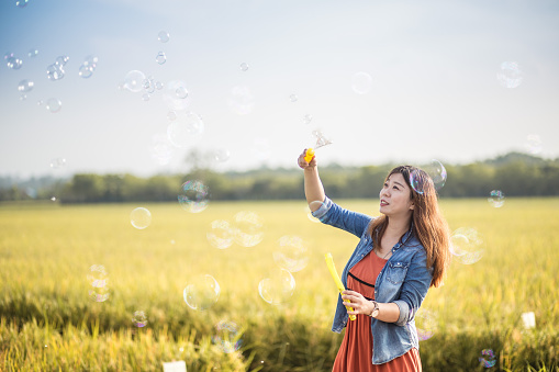 An Asia Chinese woman having fun playing soap bubble at paddy field at sunny weekend.