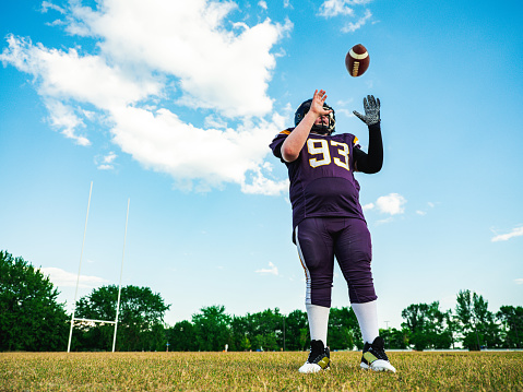 Blonde Junior Football player getting during game practice at the outdoor field. He is catching a ball in the air.