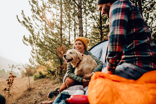 Photo of a young couple and their dog camping in the woods on a beautiful autumn day; spending time outdoors and appreciating nature.