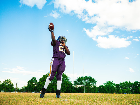 African American Junior Football player getting during game practice at the outdoor field. He is catching a ball in the air.