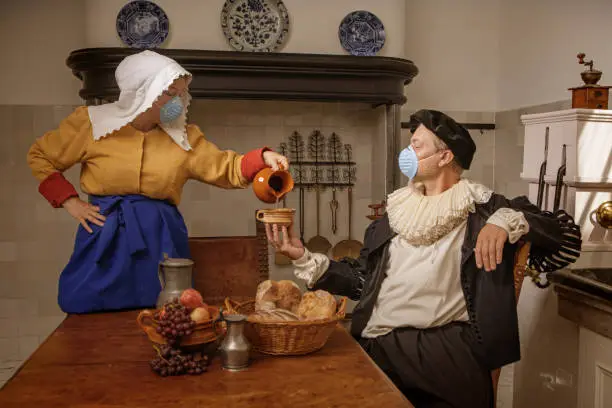 Portrait of a beautiful historical dutch milk maid and a nobleman wearing historically correct outfits in a typical townhouse kitchen during covid-19