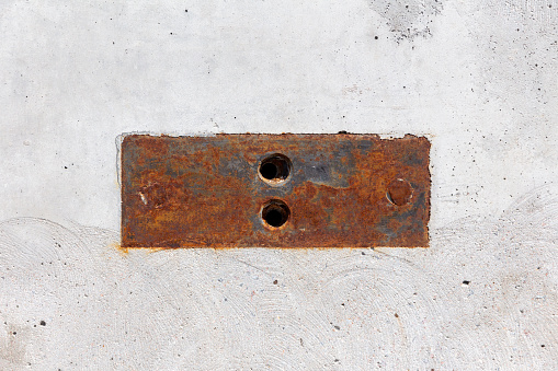 Rusty steel plate with two holes in a concrete wall. Industrial background