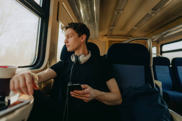jeune homme sur un train utilisant le téléphone portable - telephone window mobile phone addiction photos et images de collection