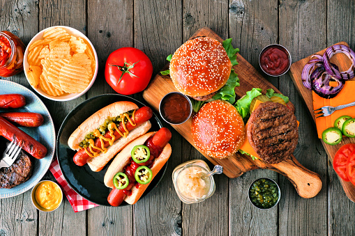 Summer BBQ food table scene with hot dog and hamburger buffet. Above view over a rustic wood background.