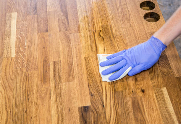 istock Person working, rubbing oiling with linseed oil natural wooden kitchen countertop before using. Solid wood butcher block countertop maintenance concept. 1254095909