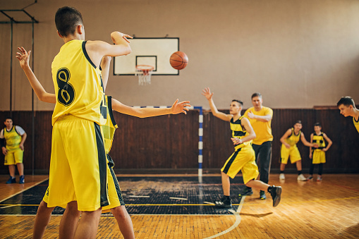 Group of men, teenage boys basketball players on training indoors with their coach.
