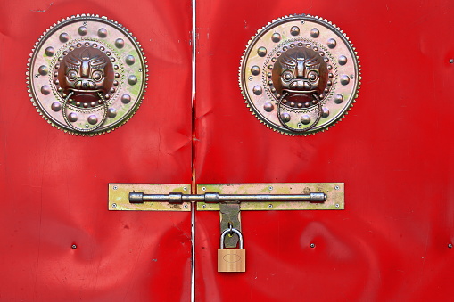 Red sheet metal door closed-brass doorknobs of foo dogs or lions-padlocked latch. Qianfo-Thousand Buddha Grottoes area of Mati Si-Horse Hoof Temple. Sunan Yugur Autonomous county-Zhangye-Gansu-China.