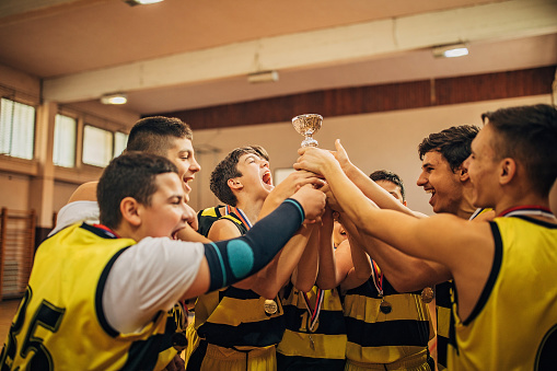 Group of boys, teenage boys basketball team celebrating wining a trophy, they are holding the trophy all together.