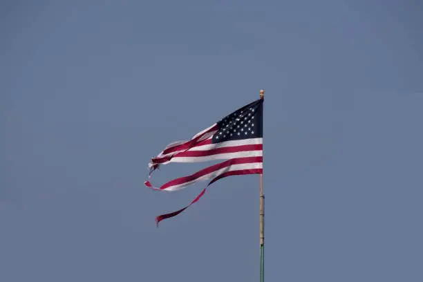 A shredded American flag against a clear blue sky seems symbolic of the divide in America.