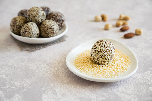 Energy ball close up. The candy is sprinkled with sesame. Homemade raw sweet with almond, cashews, peanut butter and hazelnuts on the plate on the light background.
