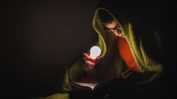 istock Teenage boy reading a book under the blanket at night 1254114561
