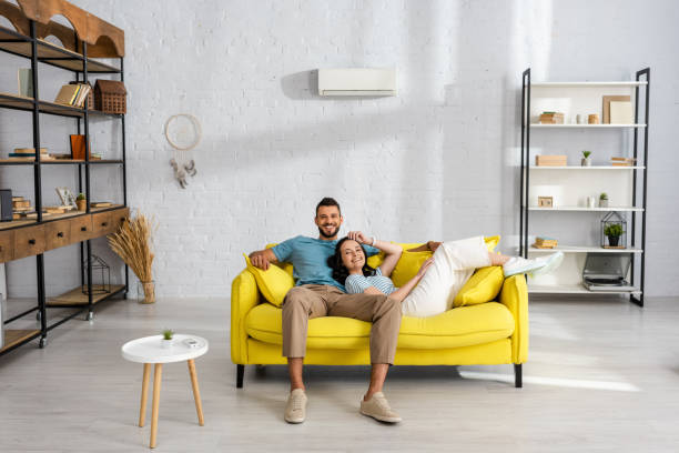 Young couple smiling at camera while sitting on yellow couch at home