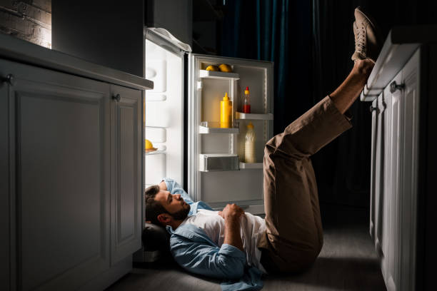 istock Side view o man sleeping on floor near open fridge at night 1254115359