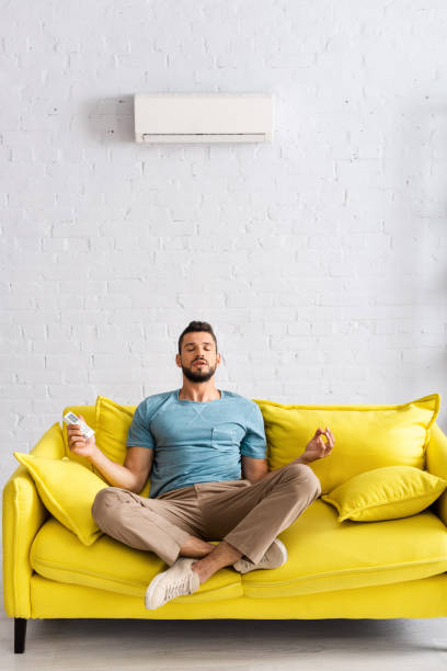 istock Handsome man meditating while holding remote controller of air conditioner on couch 1254115390