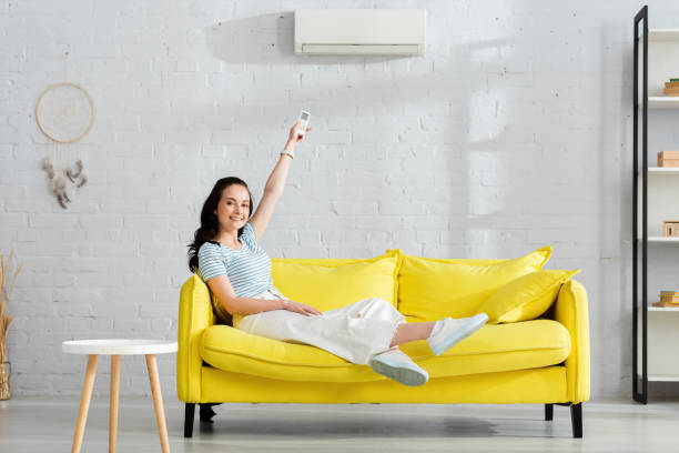 istock Beautiful girl smiling at camera while switching air conditioner with remote controller at home 1254115401