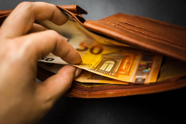 istock Woman's hand holding a black wallet with euro money. 1254116885