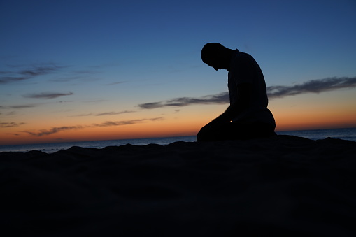 Silhouette of muslim man praying on a hilltop at sunset