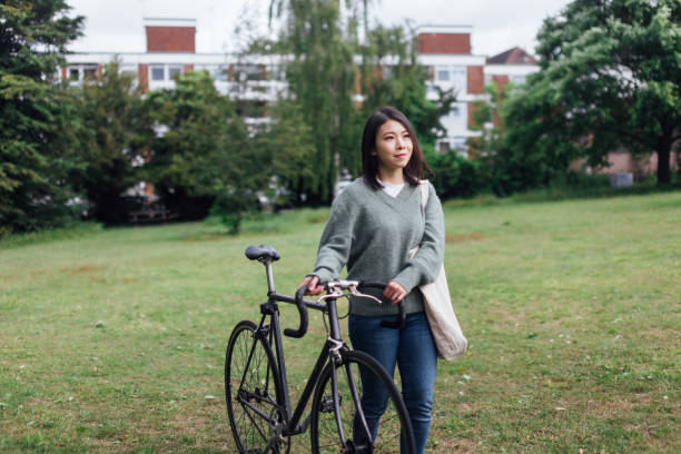 jeune femme avec le vélo détendant au parc - mental health women asian ethnicity bicycle photos et images de collection