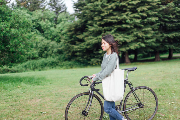 jeune femme avec le vélo détendant au parc - mental health women asian ethnicity bicycle photos et images de collection