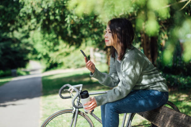 młoda kobieta z inteligentnym telefonem siedzącym na ławce w parku - mental health women asian ethnicity bicycle zdjęcia i obrazy z banku zdjęć