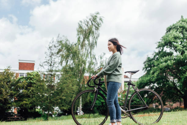 jeune femme avec le vélo détendant au parc - mental health women asian ethnicity bicycle photos et images de collection