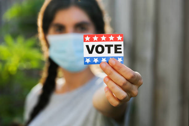 mujer joven que lleva máscara facial sosteniendo la etiqueta engomada del voto - women ethnic american culture flag fotografías e imágenes de stock