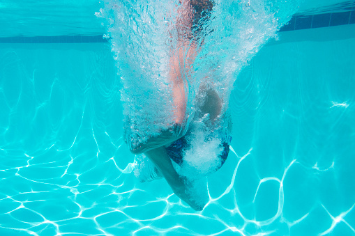 This underwater photo shows the moment after entry into a clear swimming pool when doing a cannonball.  A envelope of bubbles encircle the jumper's entire body.