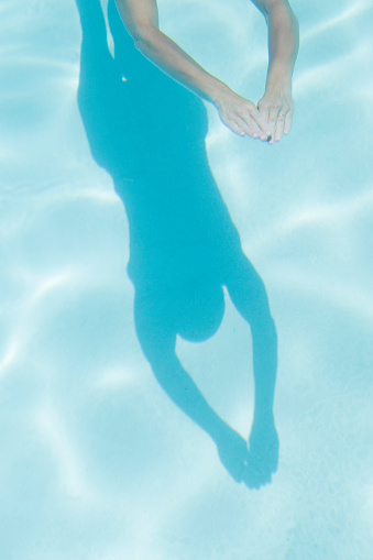 The shadow of a passing woman swimmer is reflected from the bottom of this swimming pool.  Also visible are the woman's arms.  Ripples on the waters surface reflect the bright sunshine.