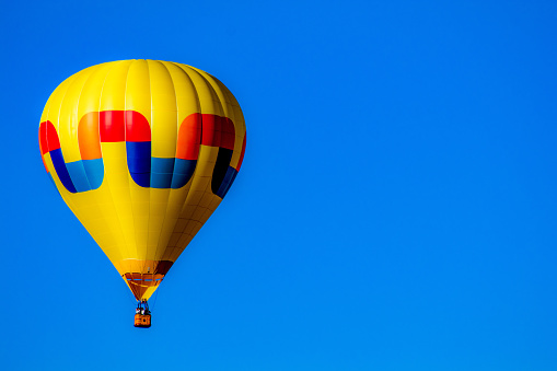 A hot air balloon floats against clear blue sky.