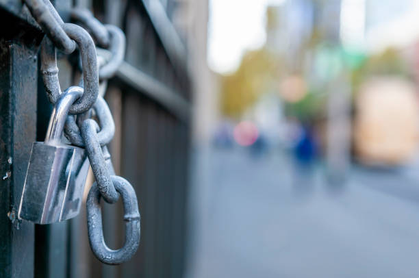 Padlock and chain slung on a gate along a sidewalk. All components are made of metal. Selective focus or shallow depth-of-field image.