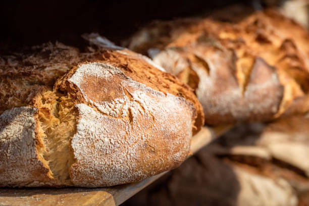 sauerteigbrot auf holzregalen. bäckereiregal mit goldenem krustenbrot - brotlaibe stock-fotos und bilder