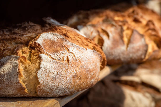 pão azedo em prateleiras de madeira. prateleira de padaria com pão de crosta dourada - comidas e bebidas artesanais - fotografias e filmes do acervo