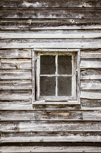 Architectural detail of a small, white, old, wooden, 4 pane barn window weathered over time.