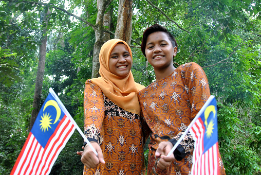 Muslim Indian ethnicity sisters are feeling cheerful spending leisure time at nature reserve holding Malaysian flag to celebrate Independence Day which falls on 31st August.