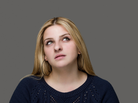 Studio shot of a young woman looking thoughtful against a grey background
