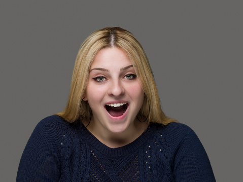 Young woman expressing great surprise against a gray background