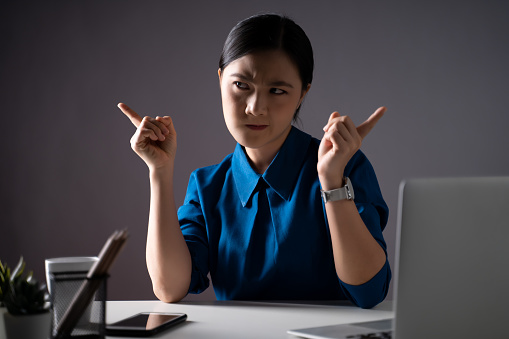 Asian woman in blue shirt feel confused, looking at copy space, working on a laptop at office. isolated on background. Low key.