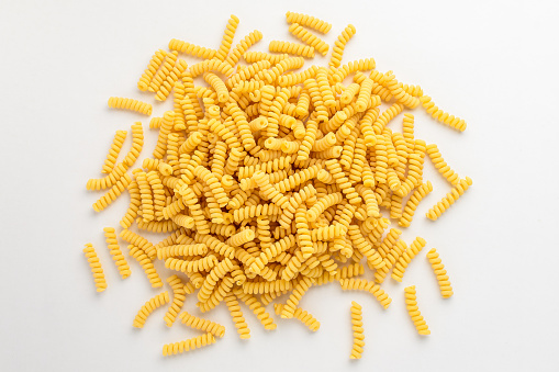 Group of dried fusilli Italian pasta in a round shape ready to be cooked, isolated on white table, with view from above